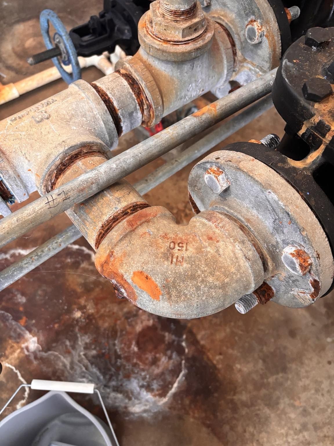Rusty industrial pipes and valves with water leaking onto a wet floor