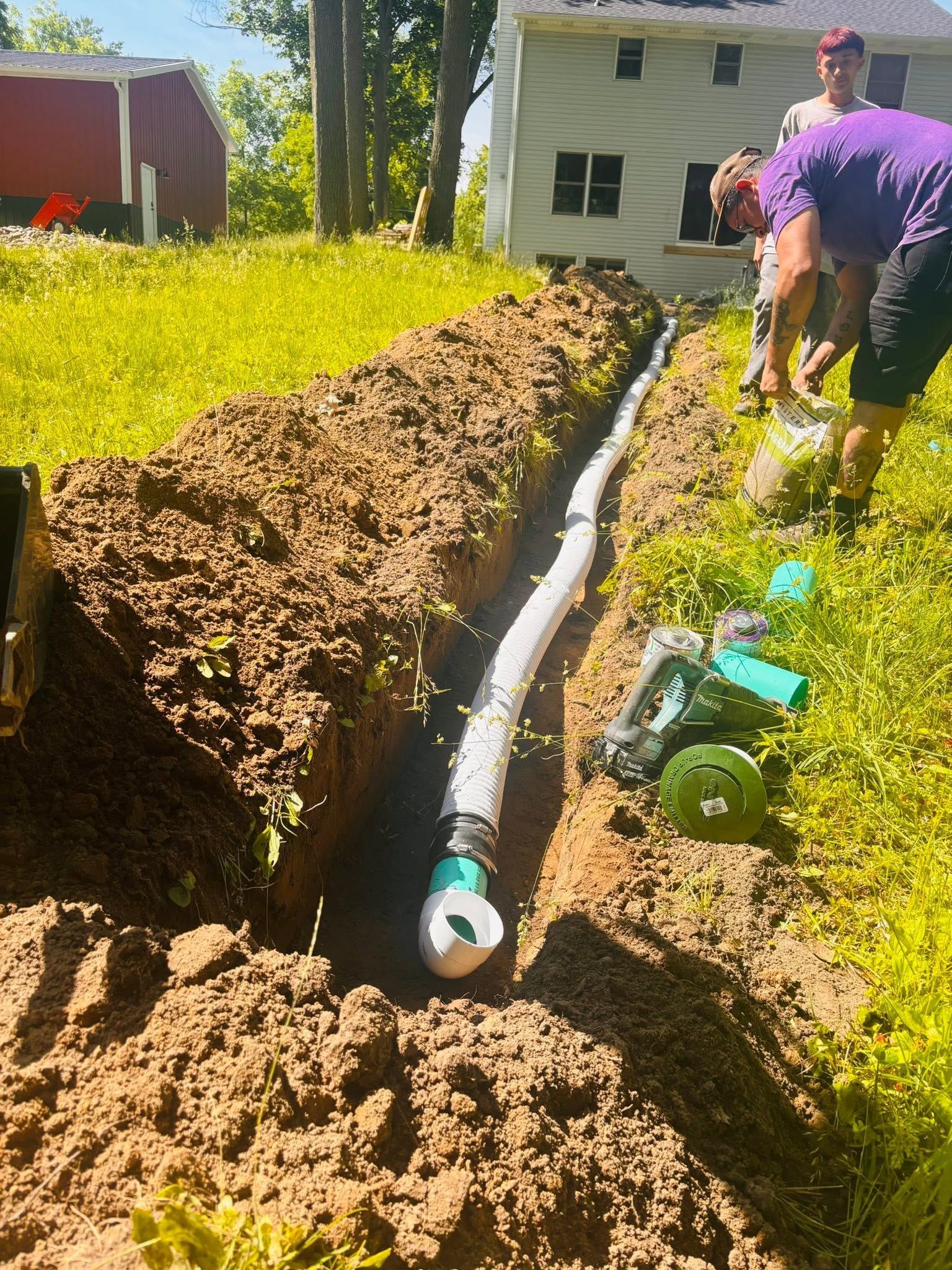 White pipe laid in a trench beside a house, with workers and a grassy yard nearby.