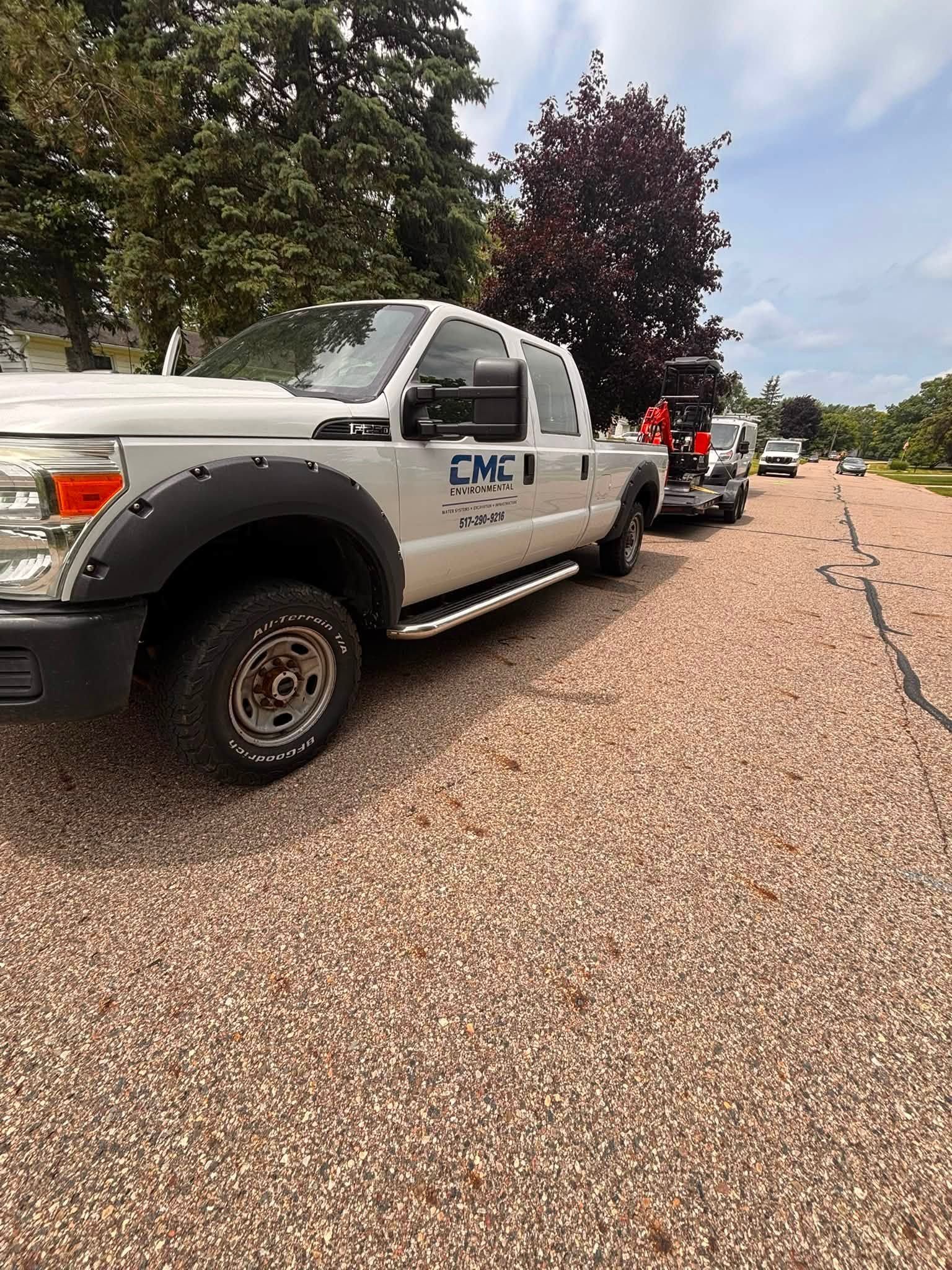 Line of parked utility trucks along a tree-lined road on a sunny day.