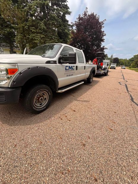 White utility trucks parked along a tree-lined road, with people visible near the vehicles.