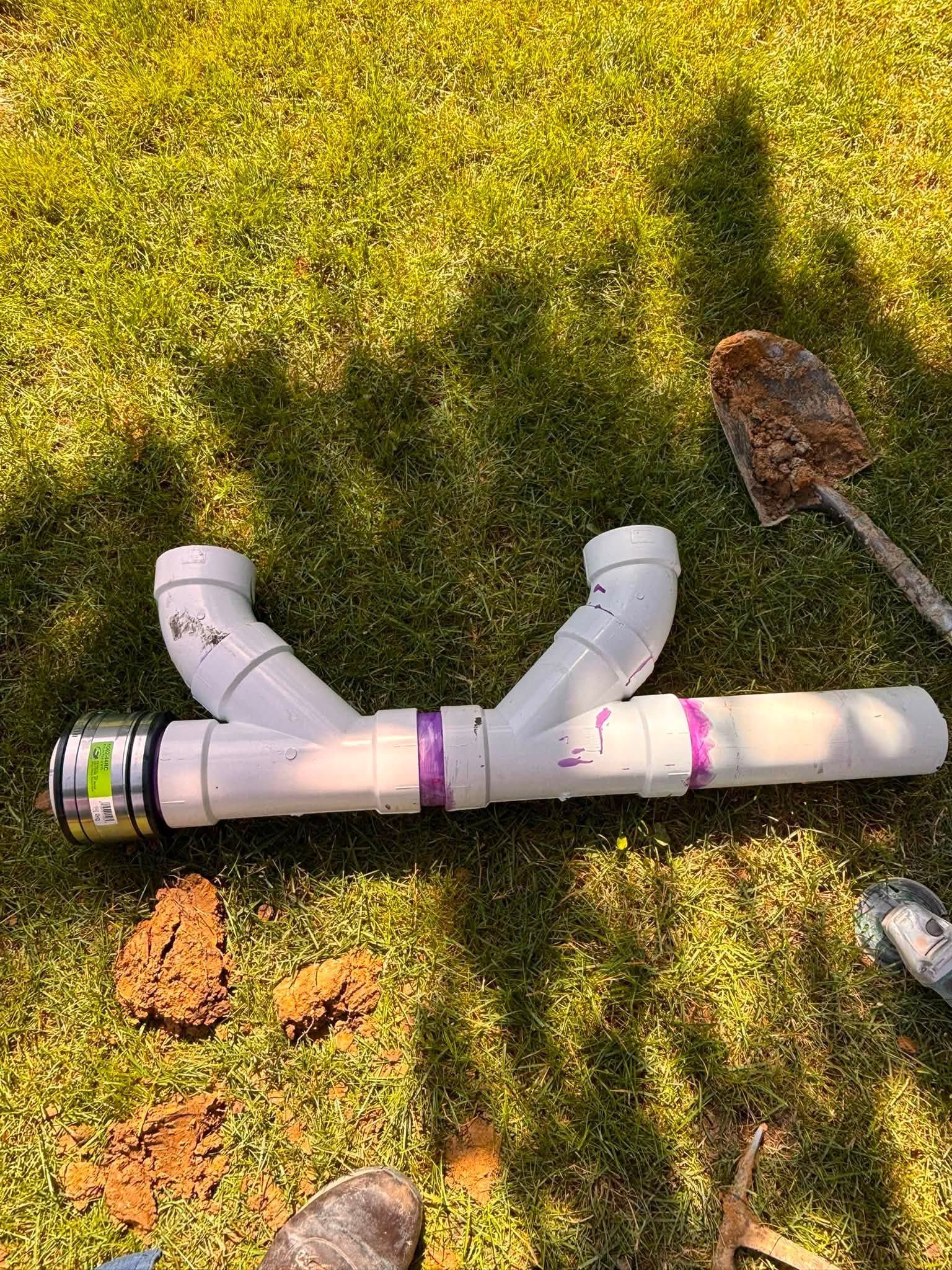 White PVC pipe assembly lying on grass beside a garden trowel and a few fallen leaves.