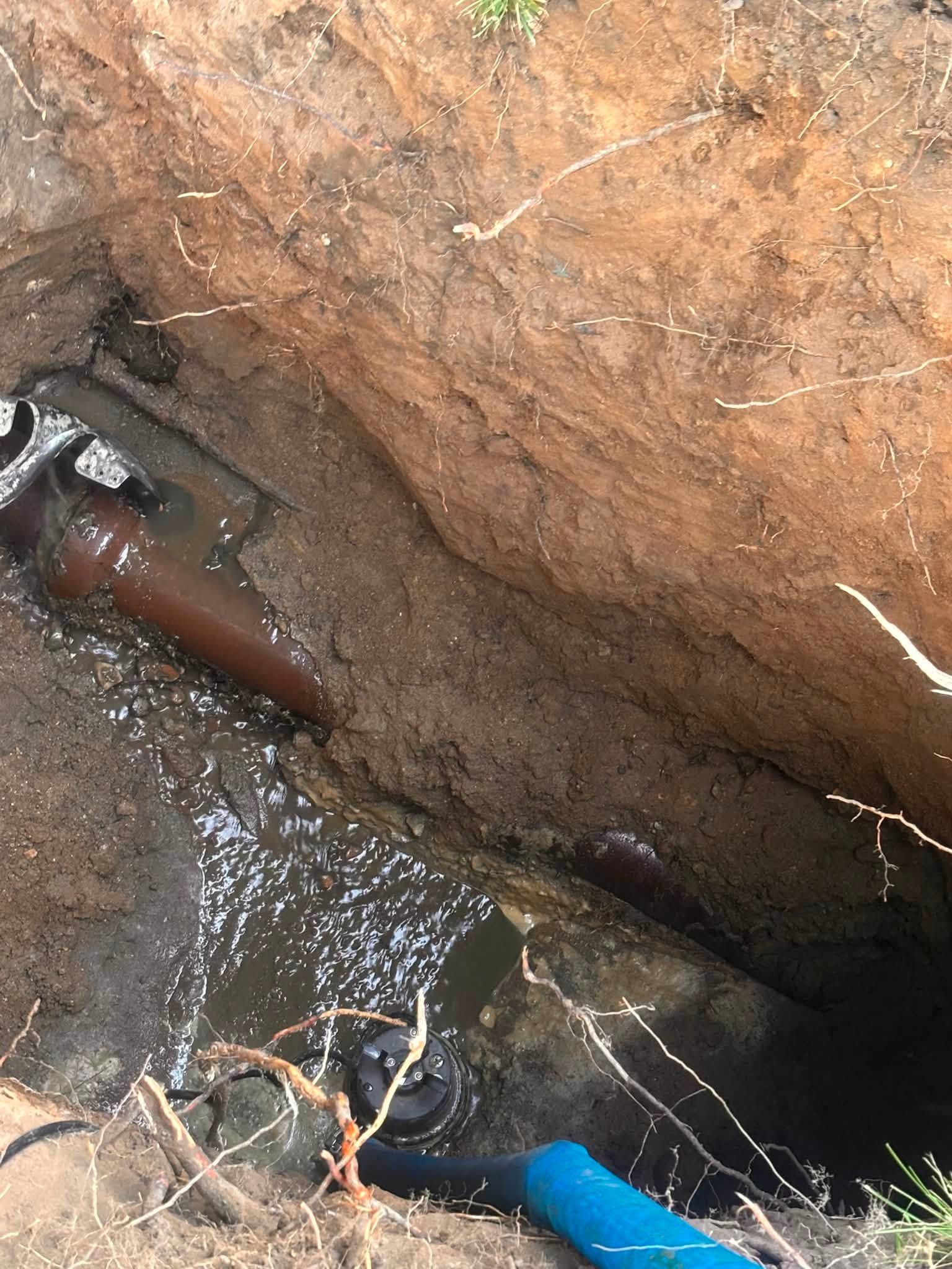 Open pit with muddy water, exposed brown rock, and a blue hose in the lower right.