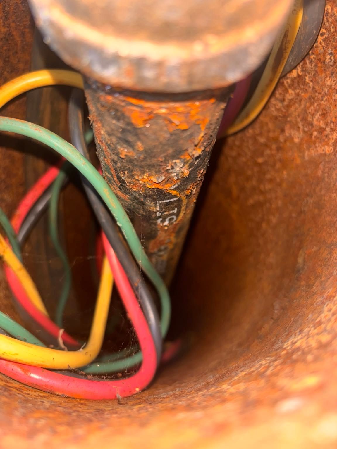 Close-up of rusted metal pipe with red, green, and yellow wires inside a brown enclosure