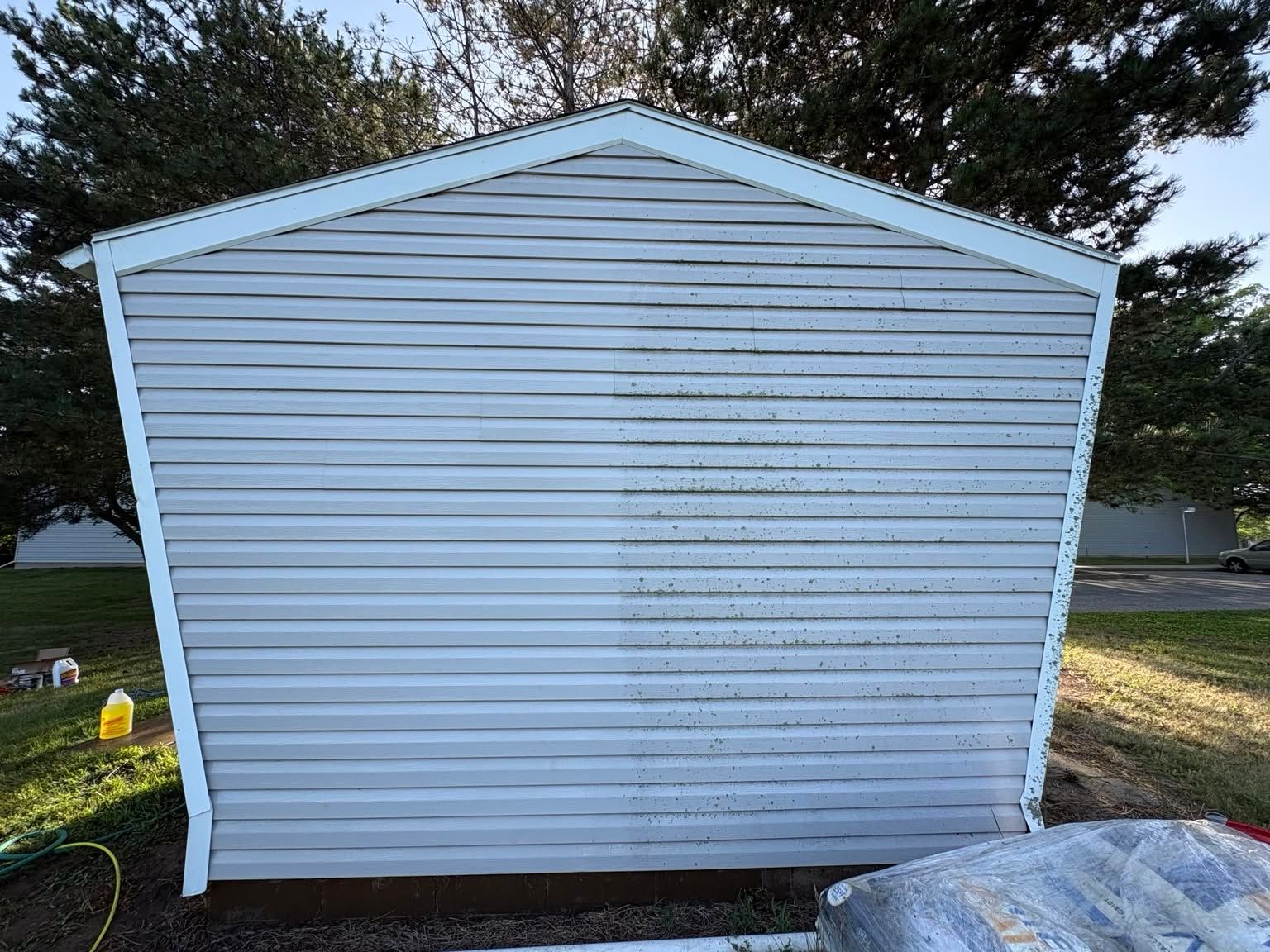 White vinyl shed with a slanted roof in a yard, with trees and grass in the background.