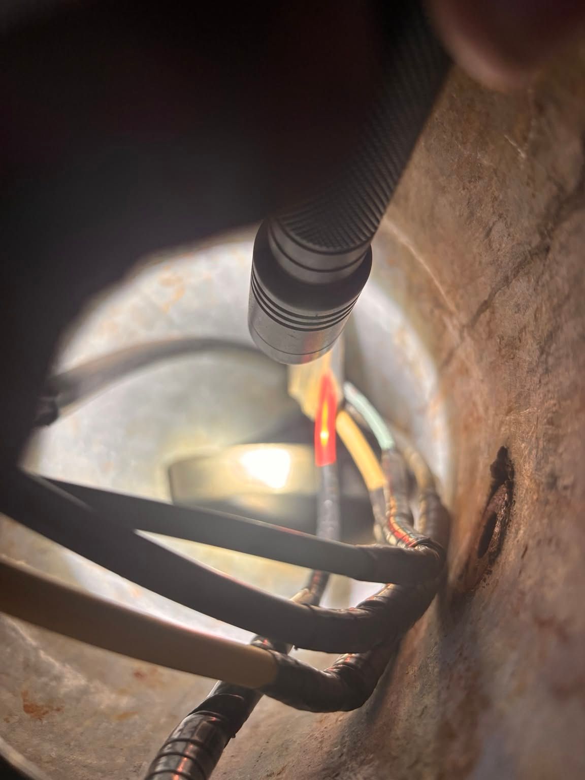 Close-up inside a metal pipe with black straps, red and yellow wires, and a flashlight beam illuminating the interior