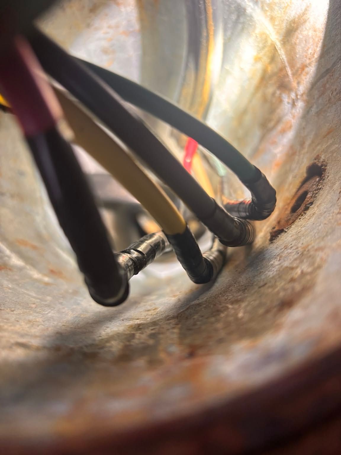 Close-up of tangled black cables inside a rusty metal tube with a bright opening in the background