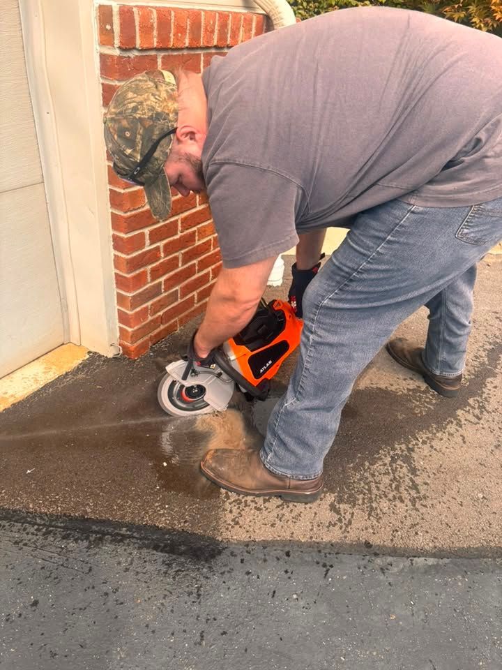 Man using a circular saw to cut concrete beside a brick wall on a wet driveway