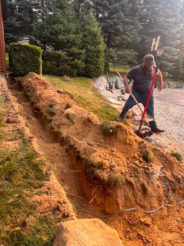 Person shoveling dirt along a steep erosion in a wooded yard after heavy rain