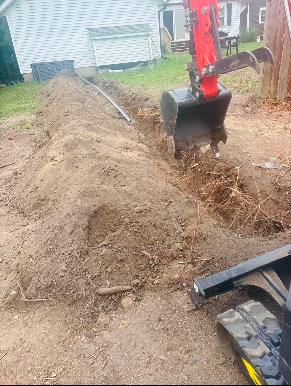 Excavator digging a trench beside a house, piling dirt along the yard.