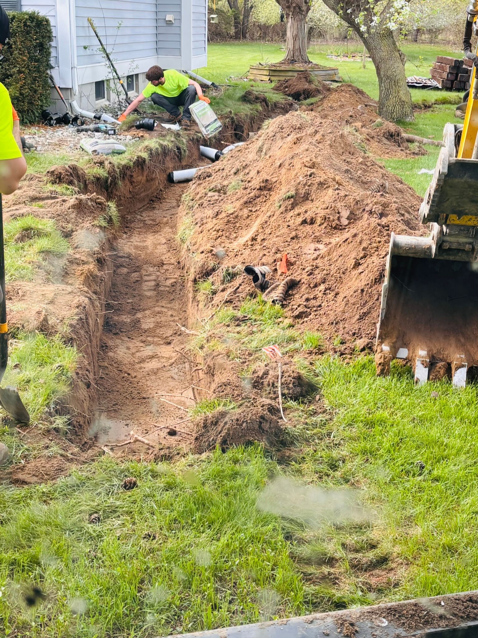 Workers digging a trench beside a house, with a large pile of dirt and a dump truck nearby