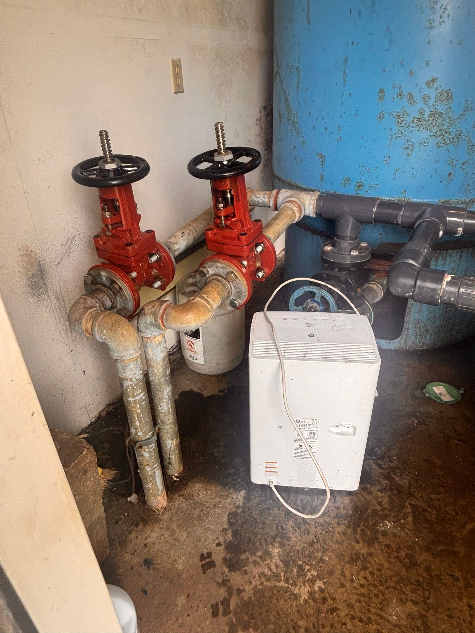 Industrial pipes and valves with a white dehumidifier in a damp utility room