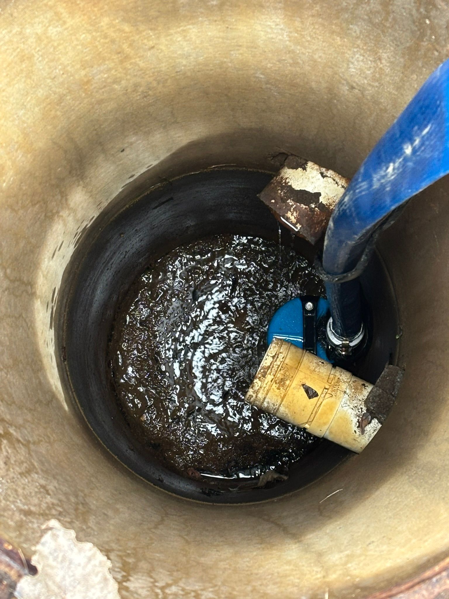 Blue hose and floating debris inside a round well or drain with dark water