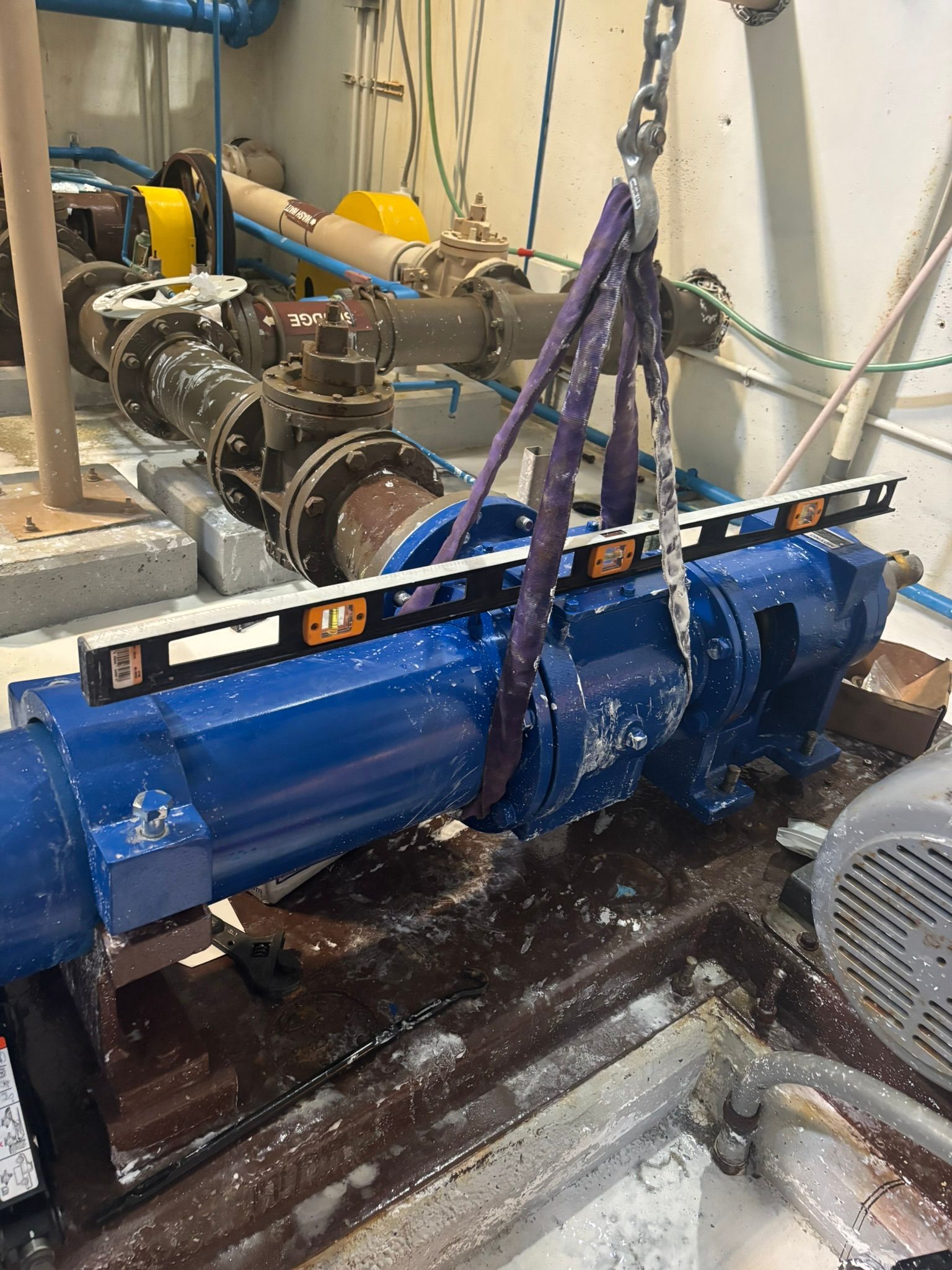 Blue industrial pump being lifted with purple straps in a factory setting