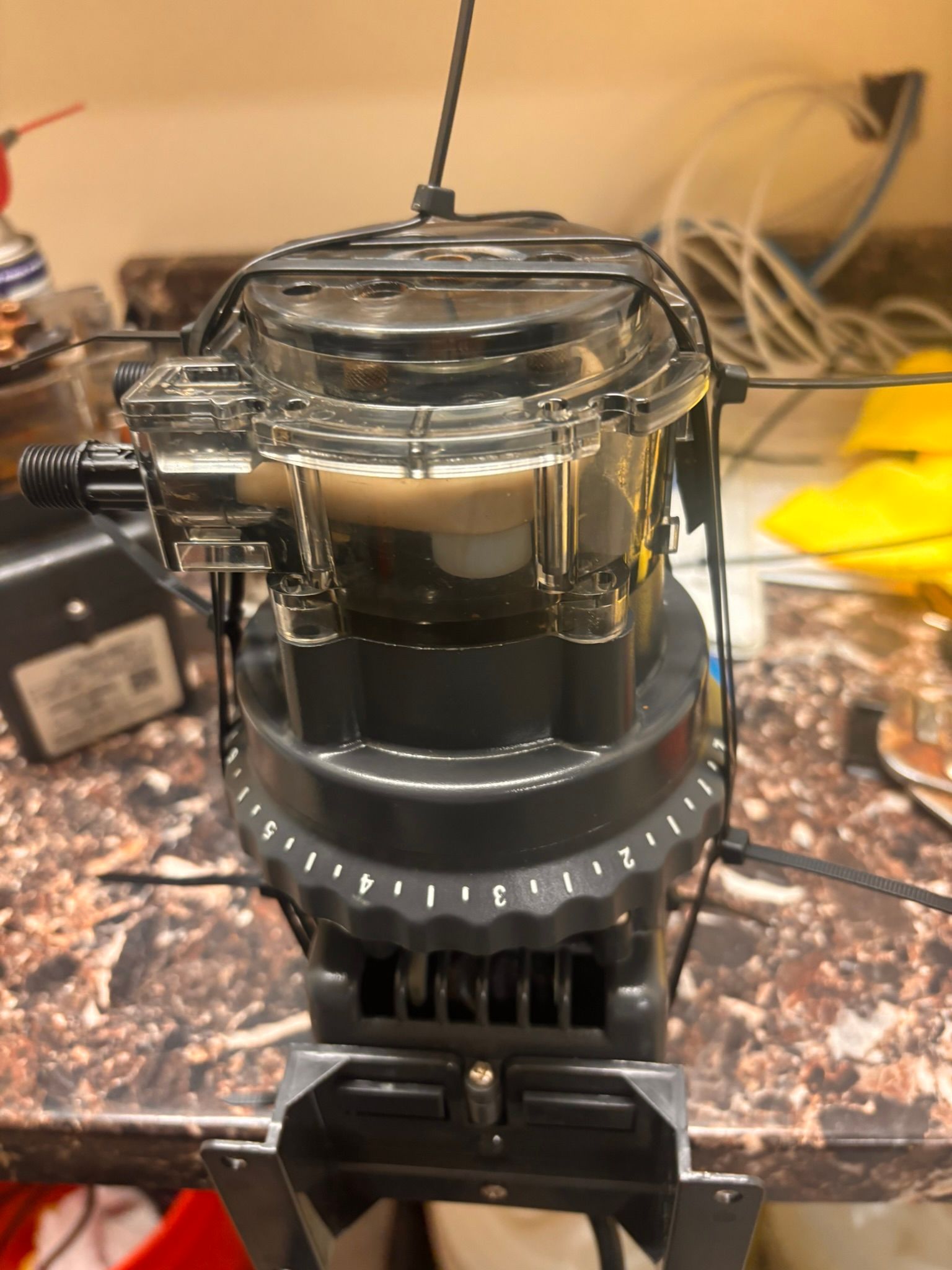 Clear-top bait aerator with dark liquid and tubing, mounted on a kitchen counter.
