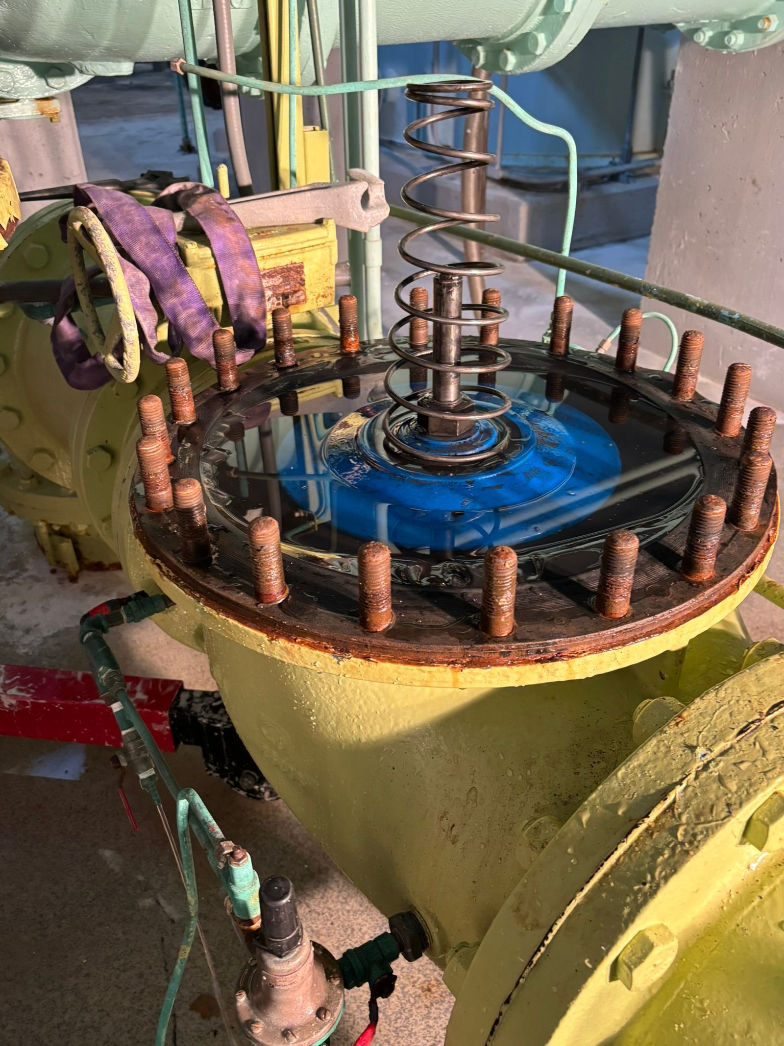 Industrial machine with a circular yellow housing, rusty bolts, and a blue central plate with a spring mechanism.