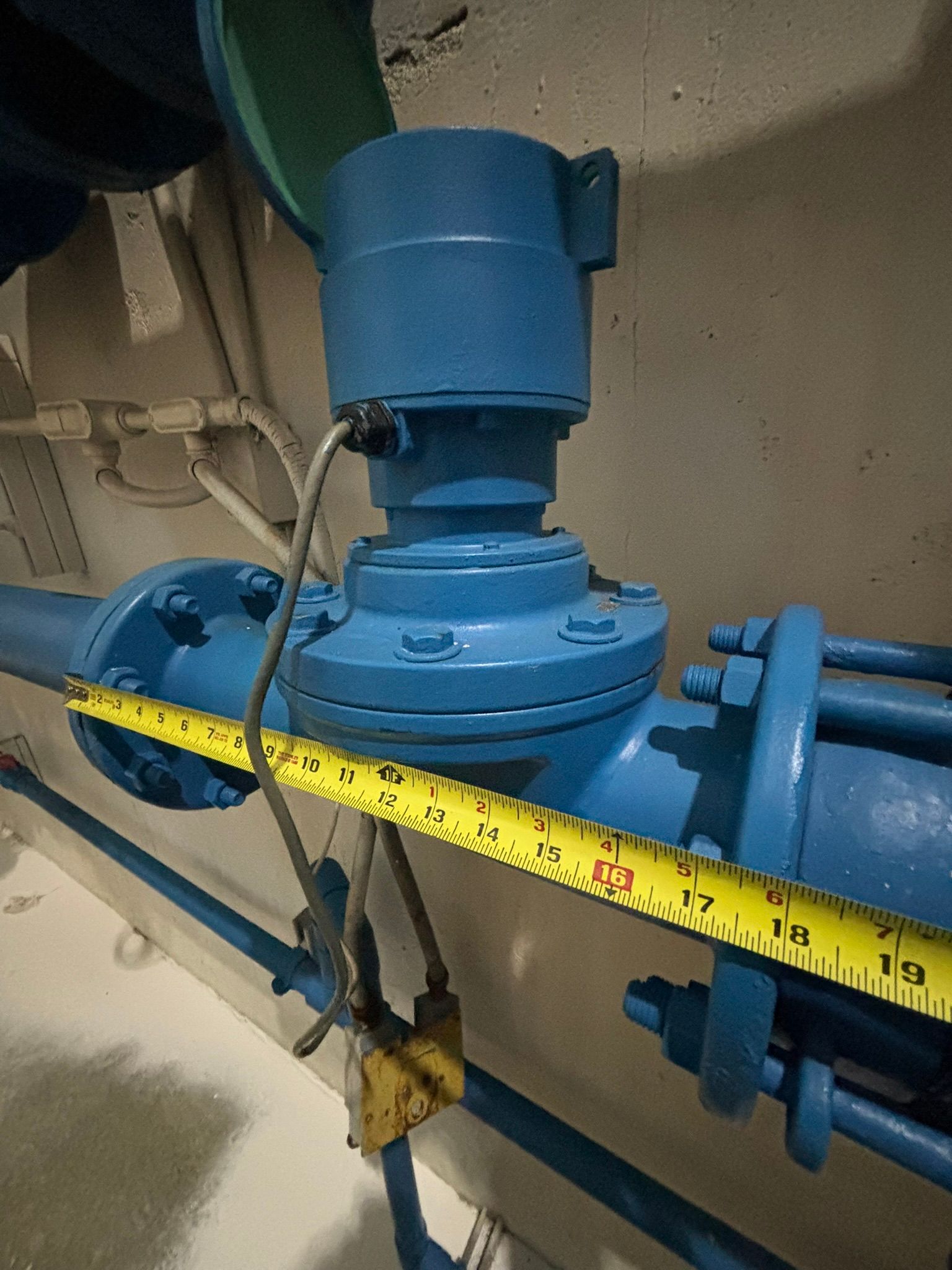 Blue industrial valve with a yellow measuring tape across it in a mechanical room