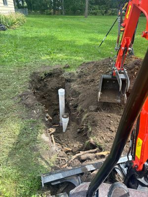 Backhoe digging a trench around a white pipe in a grassy yard
