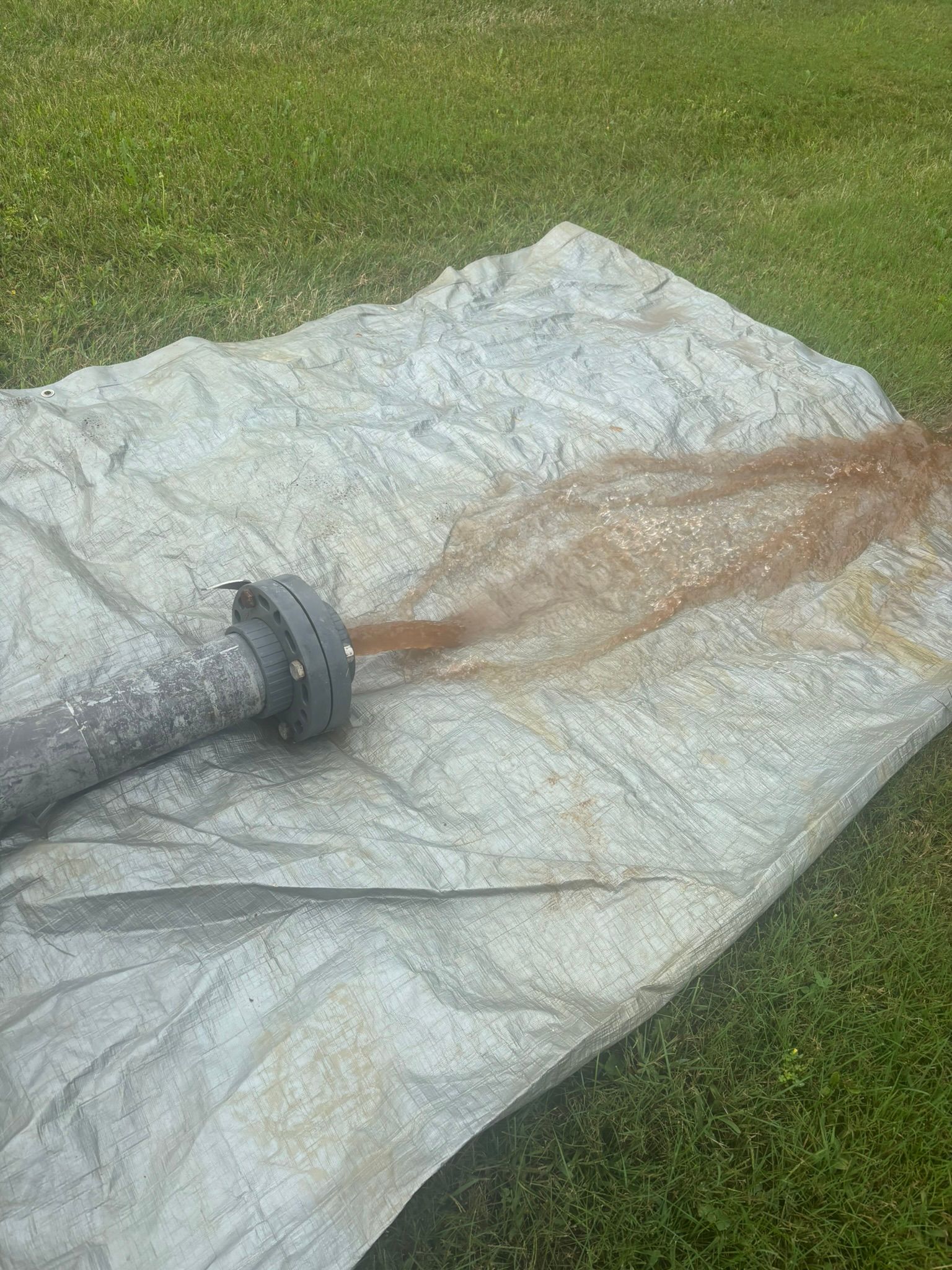 Garden hose spraying muddy water onto a white tarp on grass