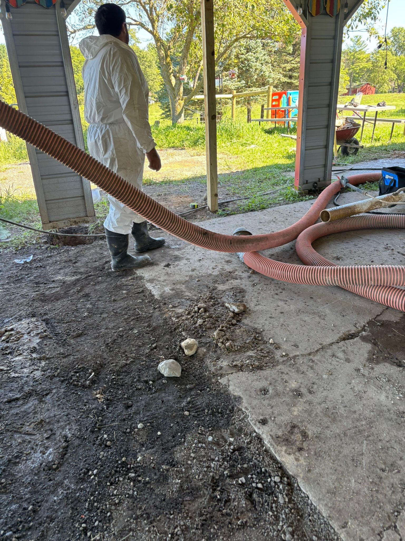 Worker in white protective suit inspecting damaged red hose at a covered outdoor site