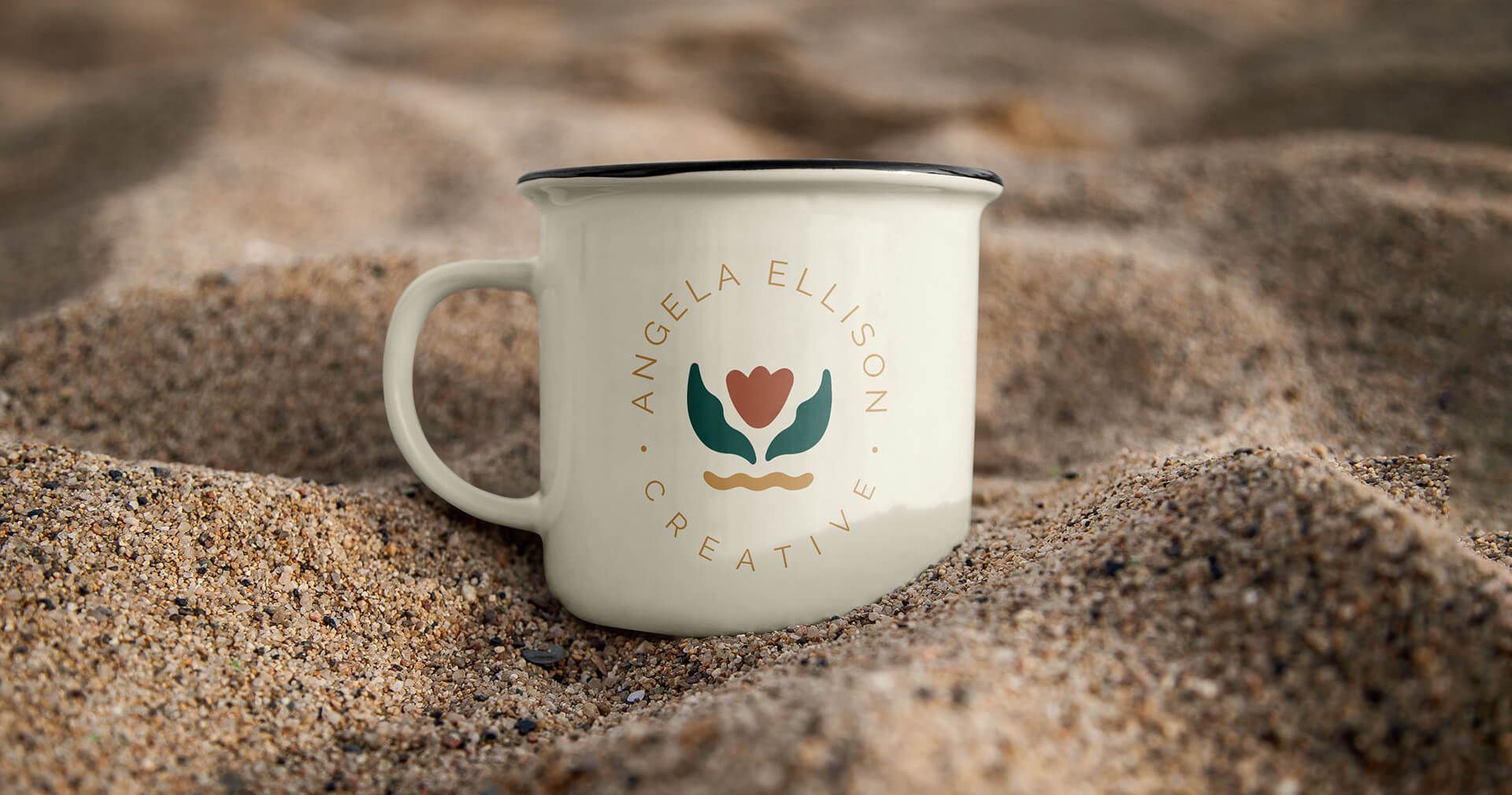 Secondary logo on a ceramic mug, sitting in the sand for woman-owned business.