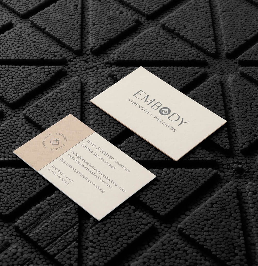 Business cards for woman-owned business, front and back, shown on top of a textured, black gym floor.