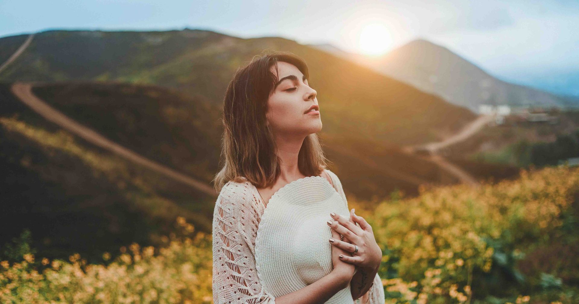Female founder at the top of a mountain with the sunrise to her back and wildflowers on all sides.