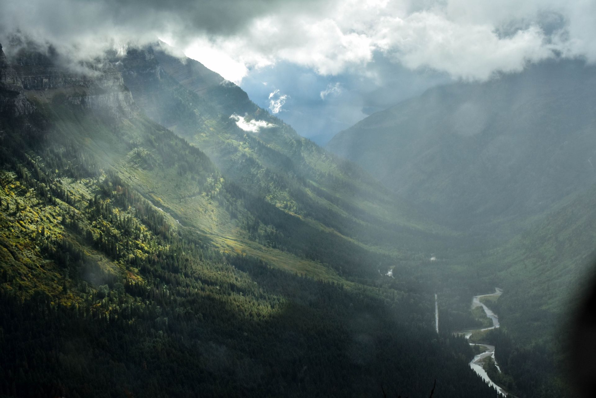 Valley of green lit up by rays of sun coming through the gray clouds above.