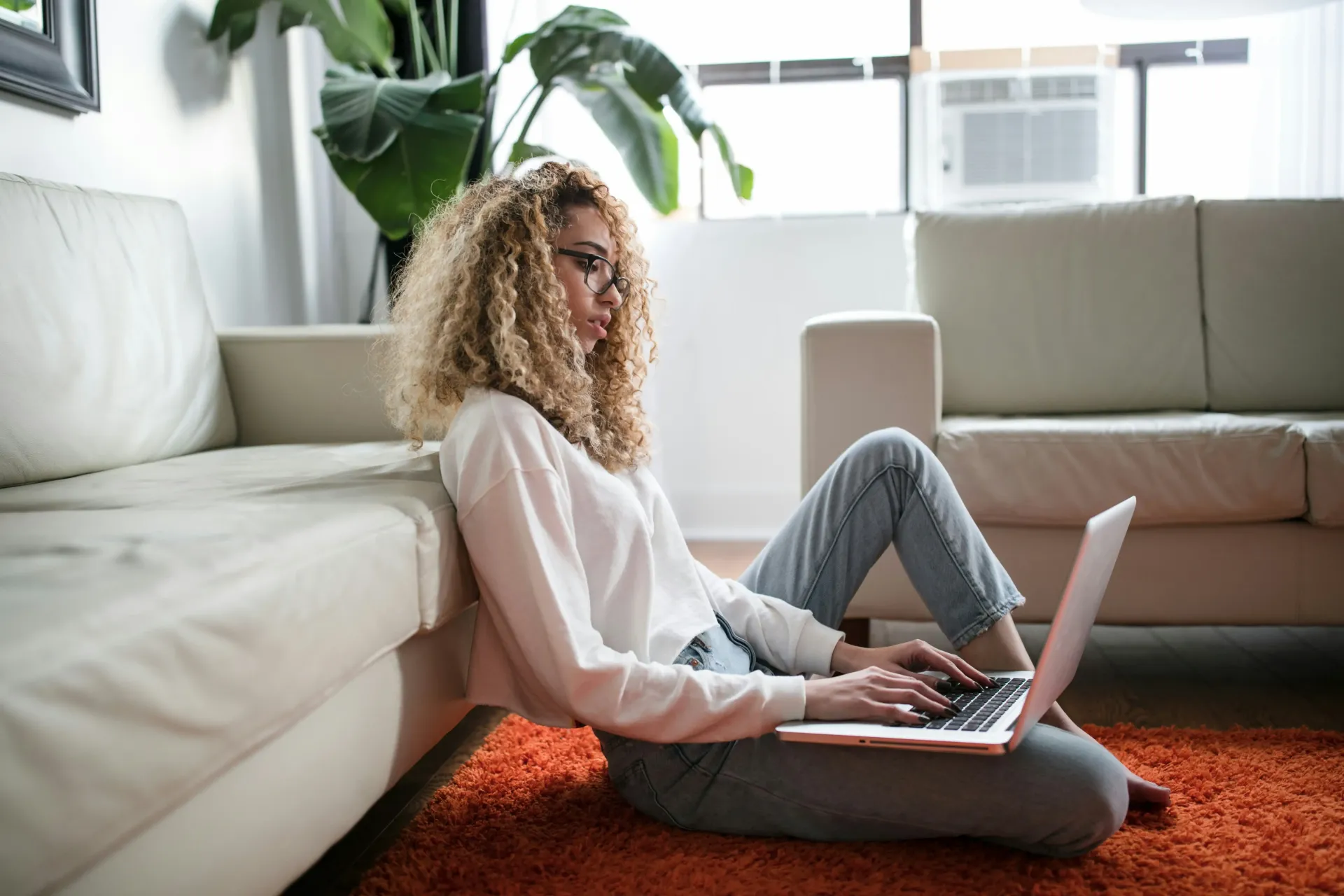 Woman sitting in front of a couch on the carpet with her laptop in her lap searching for design support.