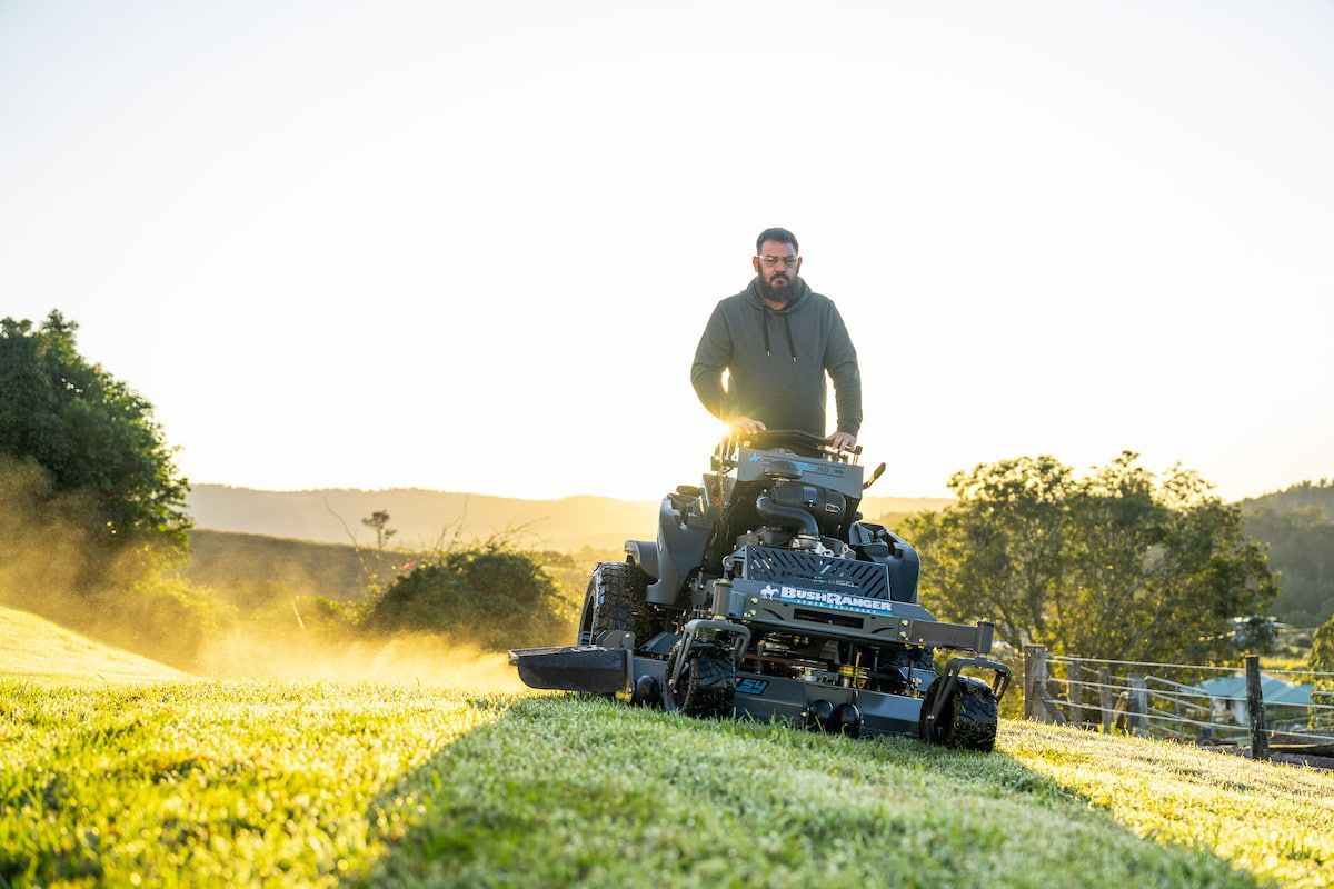 A Man Is Riding a Lawn Mower on Top of A Lush Green Field — Cheshire Machinery in Svensson Heights, QLD