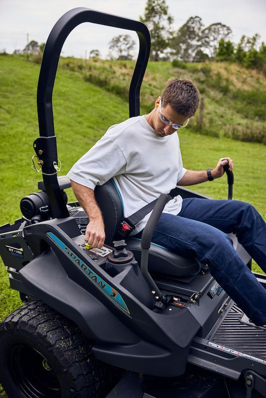 A Man Is Sitting on A Lawn Mower in A Grassy Field — Cheshire Machinery in Svensson Heights, QLD