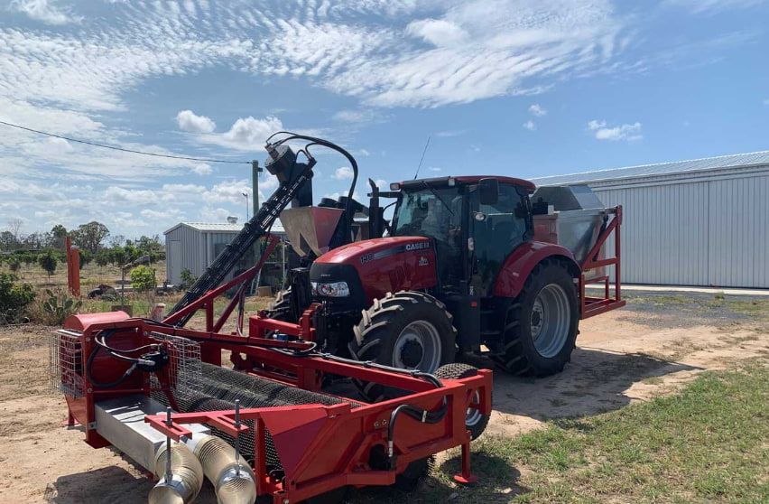 A Red Tractor Is Parked in A Field with A Trailer Attached to It — Cheshire Machinery in Bundaberg, QLD