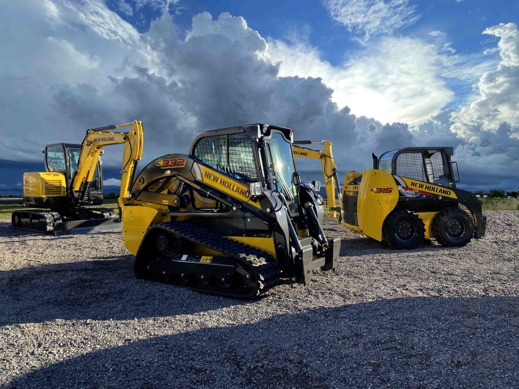 A group of construction vehicles are parked in a gravel lot.