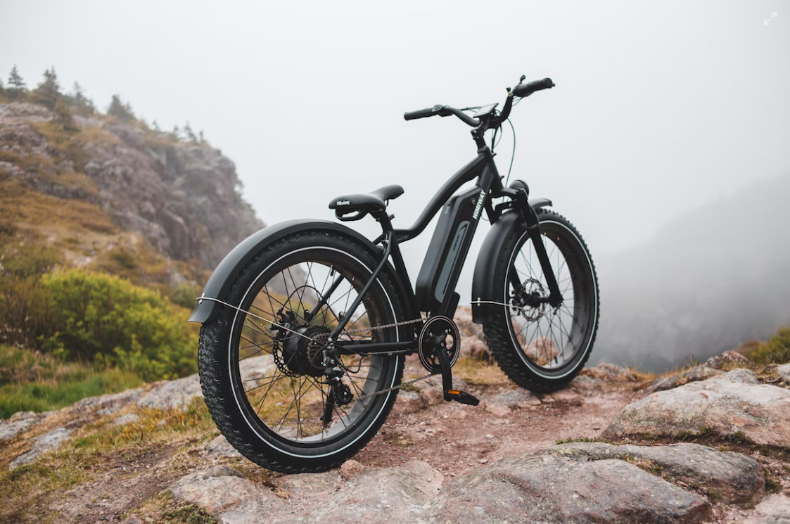 A black electric bike is parked on top of a rocky hill.