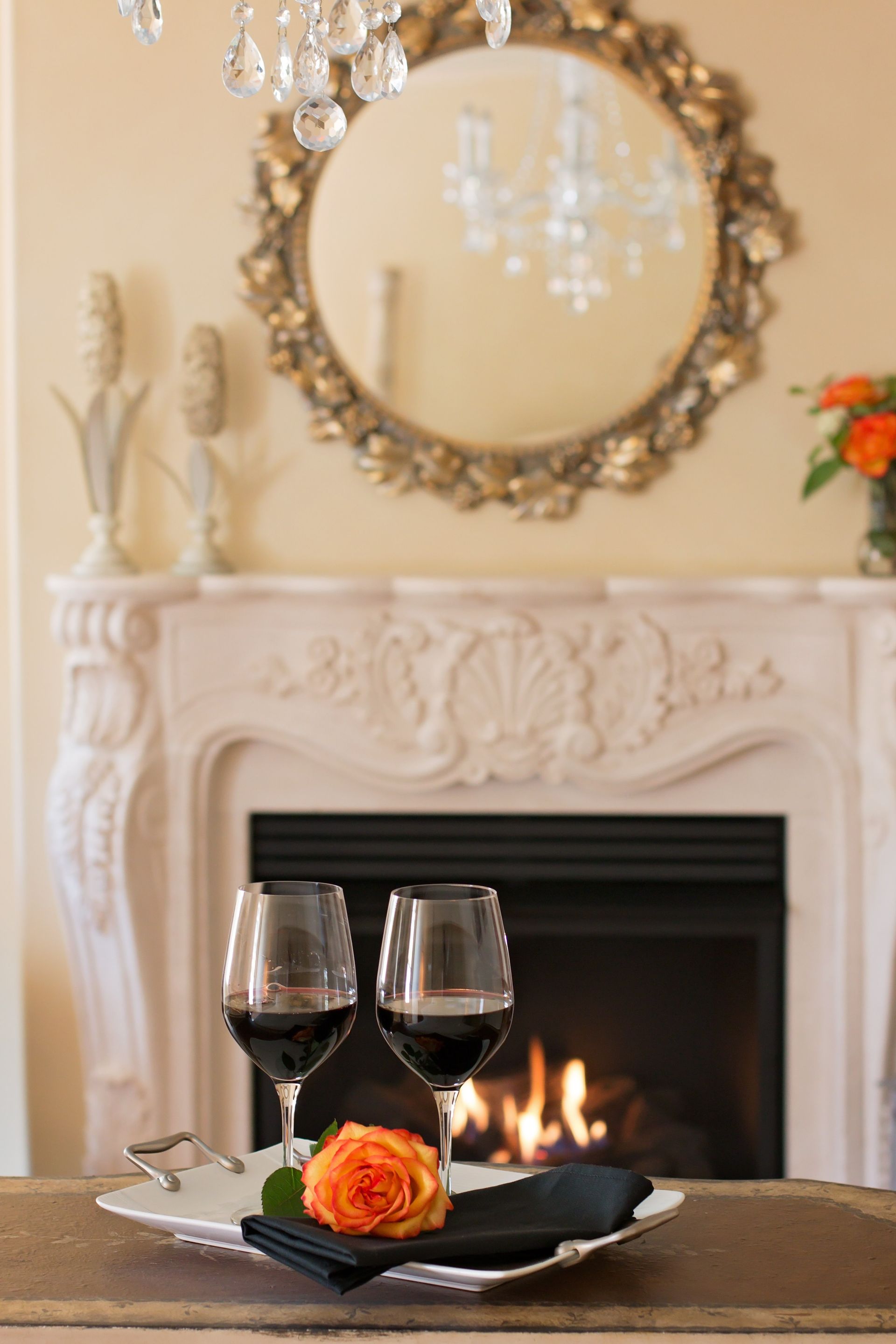 Two glasses of wine are on a plate in front of a fireplace.