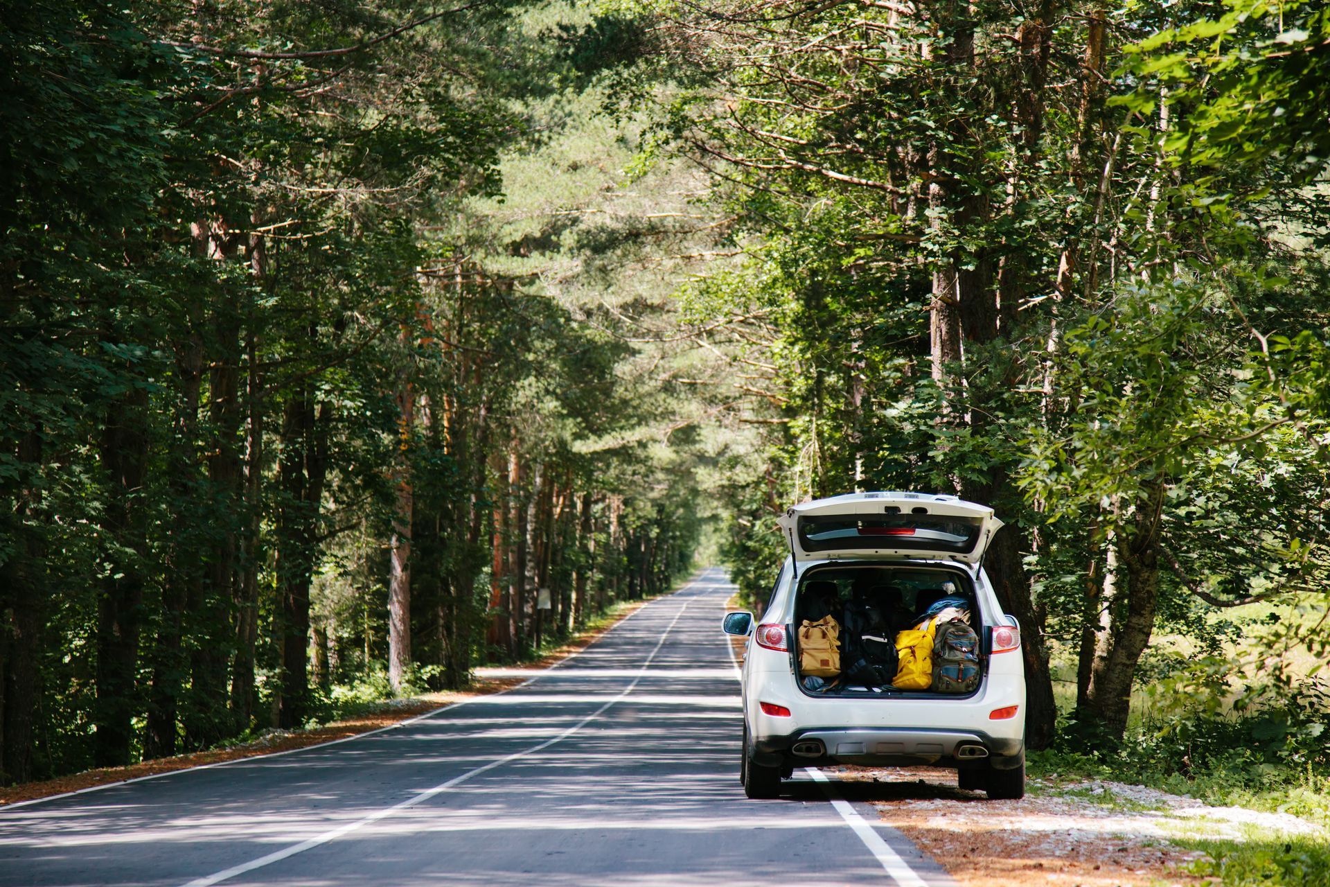 A car with its trunk open is driving down a road.