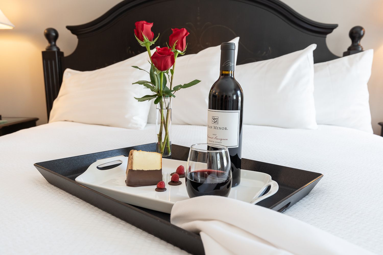 A bed with a tray of food and wine on it.