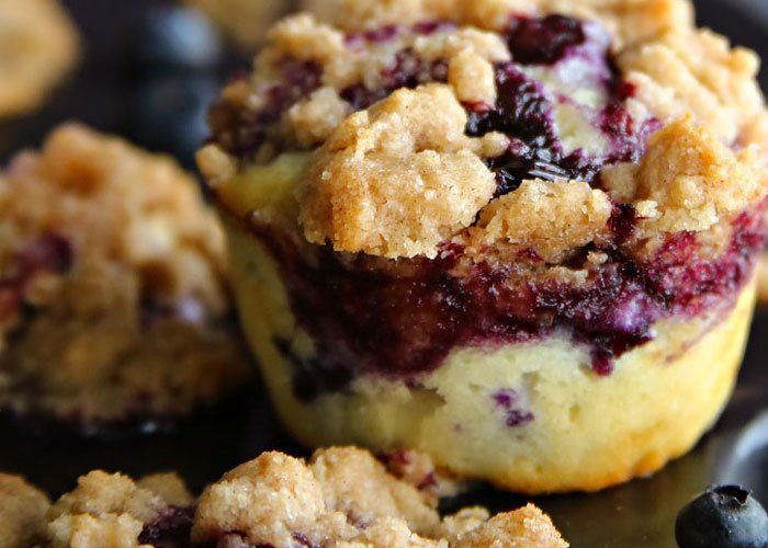 A close up of a blueberry muffin on a plate with blueberries.