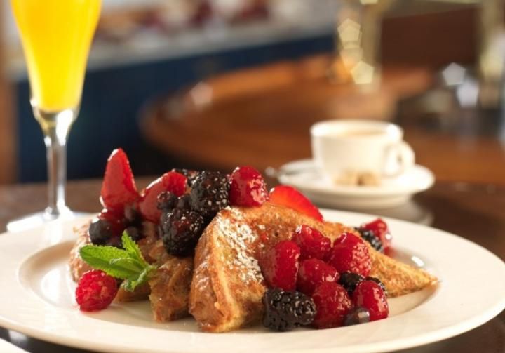 A white plate topped with french toast and berries next to a glass of orange juice