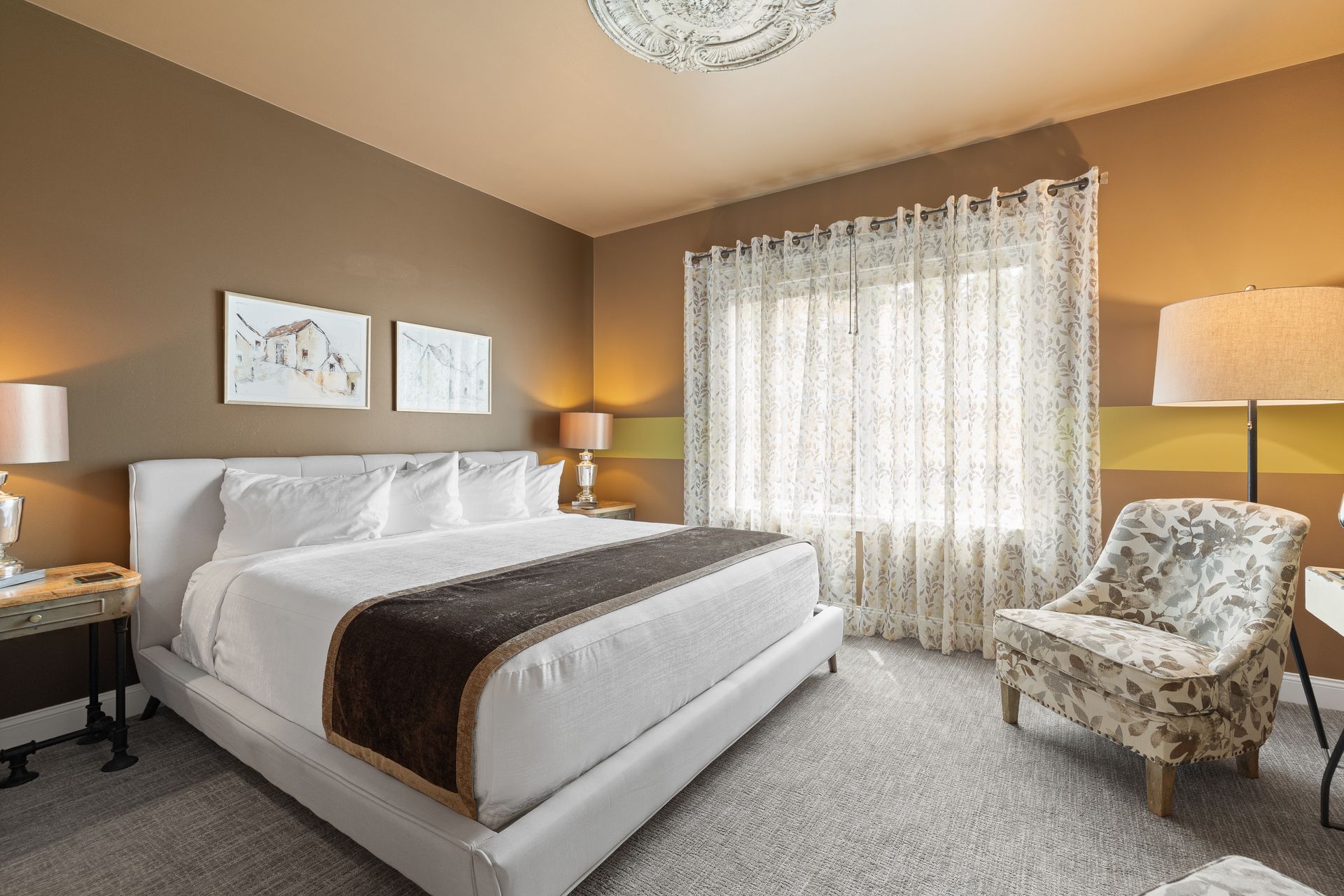 A bedroom with a large bed , chair , lamp and window.