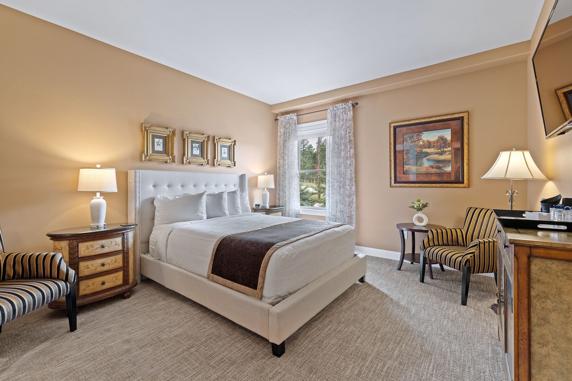 A bedroom with a bed , dresser , chairs and lamps.