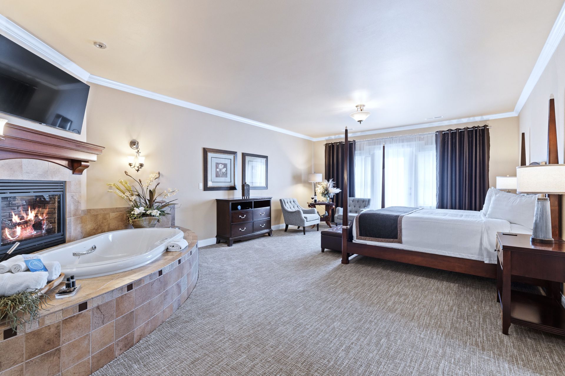 A hotel room with a king size bed , chairs , a fireplace and a jacuzzi.