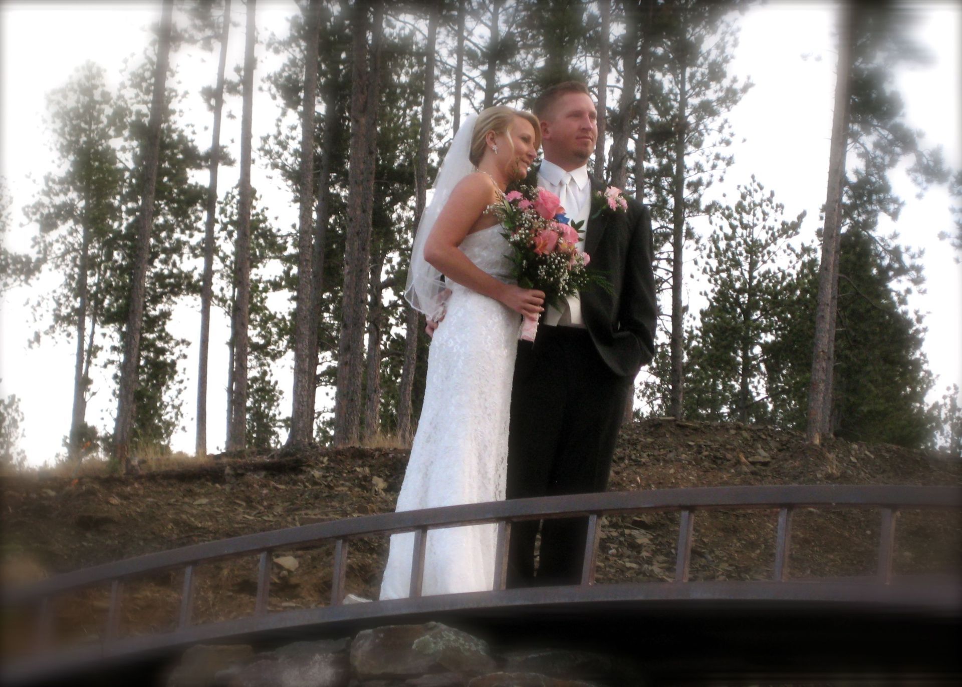 A bride and groom standing on a bridge in the woods