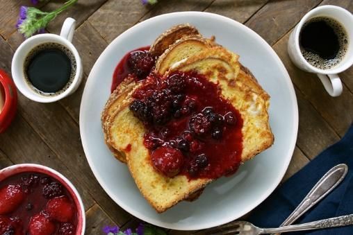 A white plate topped with french toast and berries next to two cups of coffee.