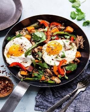 A frying pan filled with eggs , vegetables and meat.