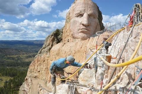 A man is working on a statue of a man on top of a mountain.