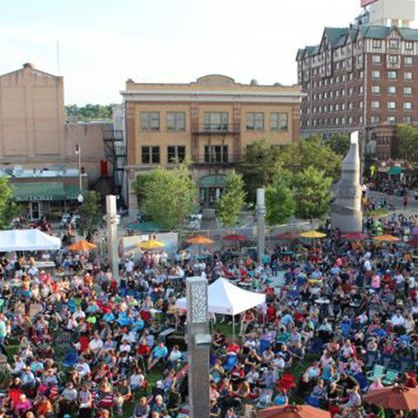 A large crowd of people are gathered in a park in front of a large building