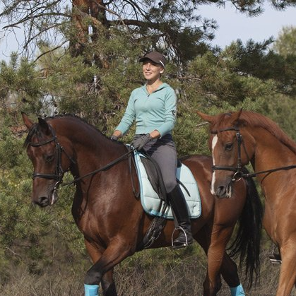 A woman is riding a brown horse with a blue saddle