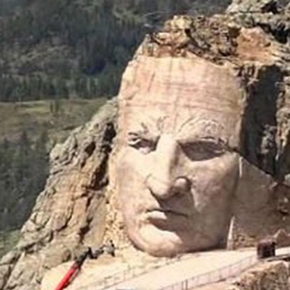 A large statue of a man 's head is sitting on top of a mountain.