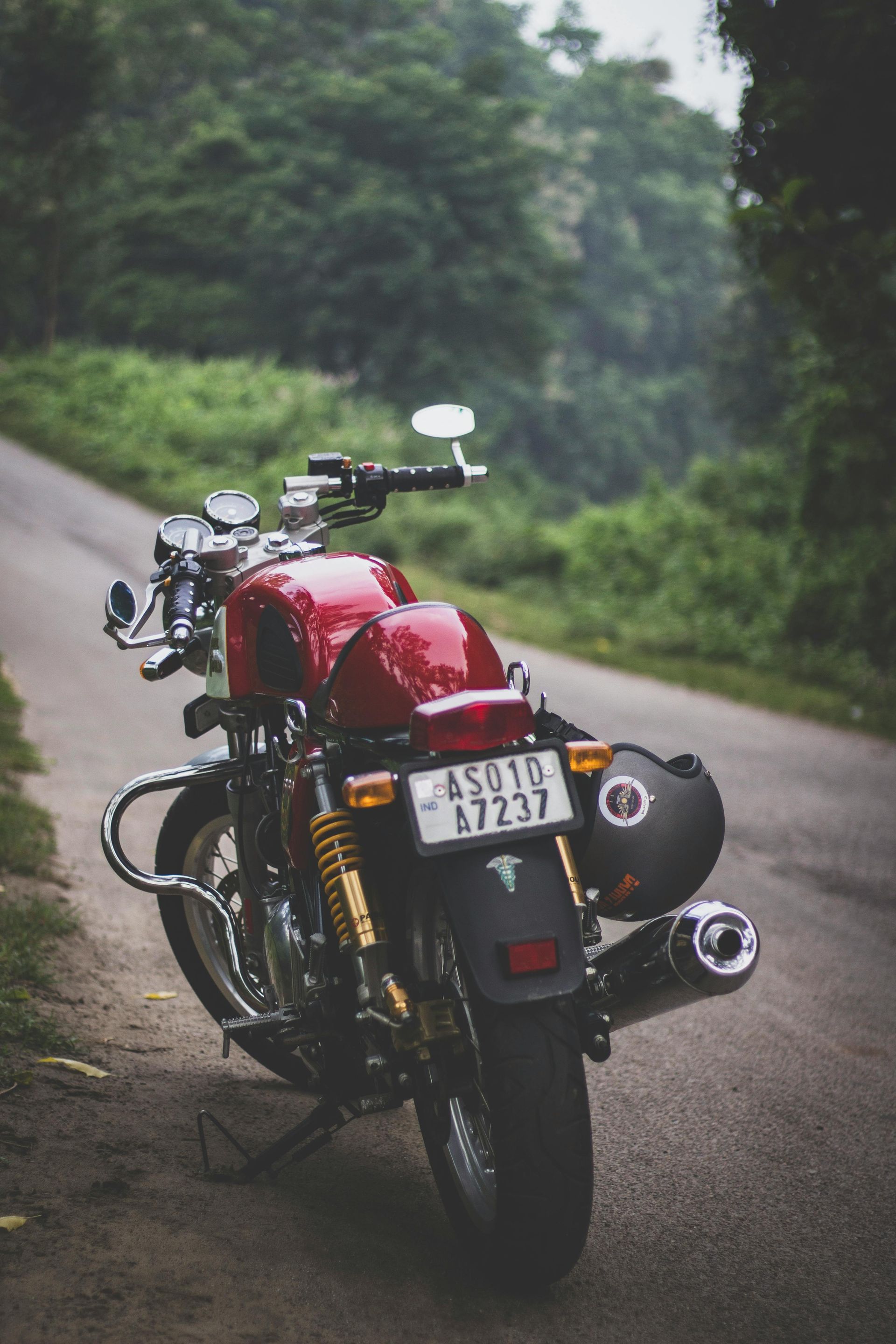 Red motorcycle parked on a road, helmet attached. Green forest in the background.