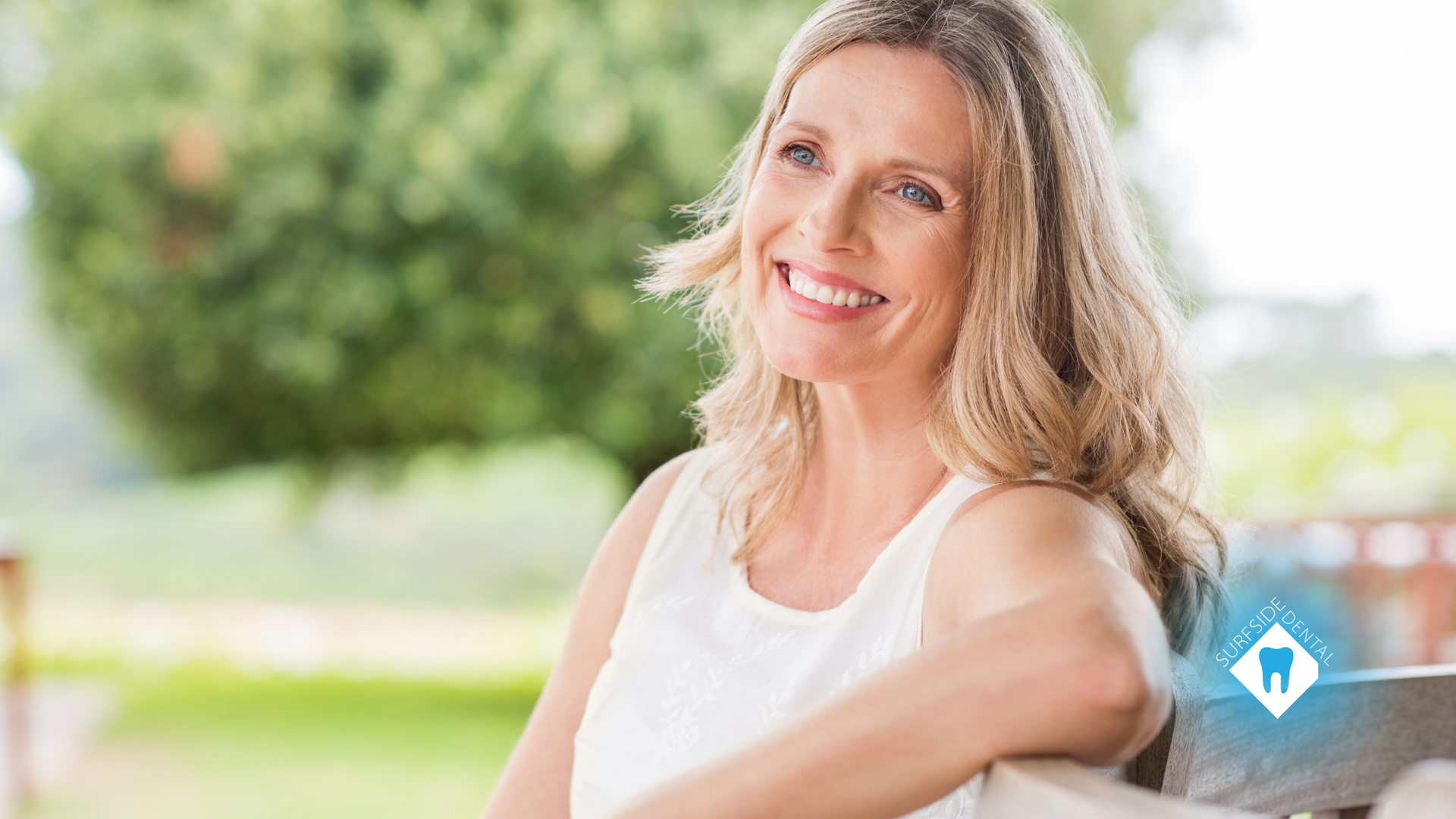 A woman is smiling while sitting on a bench in a park.